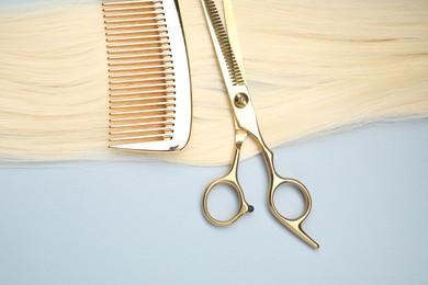 Photo of Blonde hair strand, comb and professional scissors on light grey background, top view