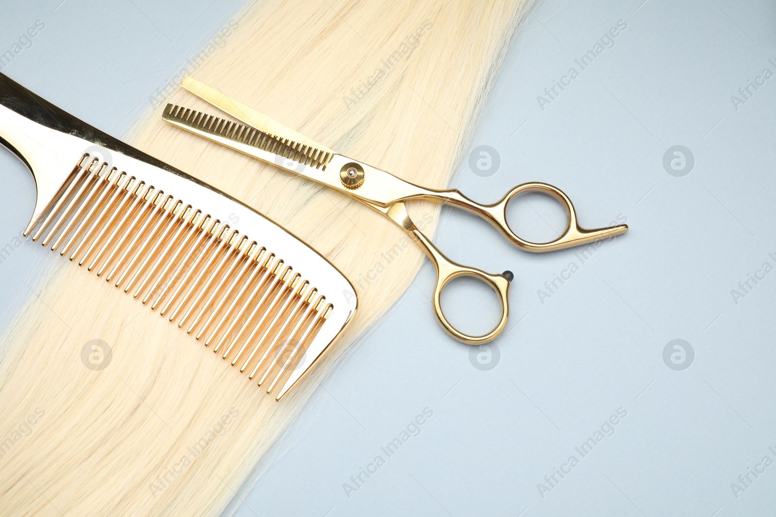 Photo of Blonde hair strand, comb and professional scissors on light grey background, top view