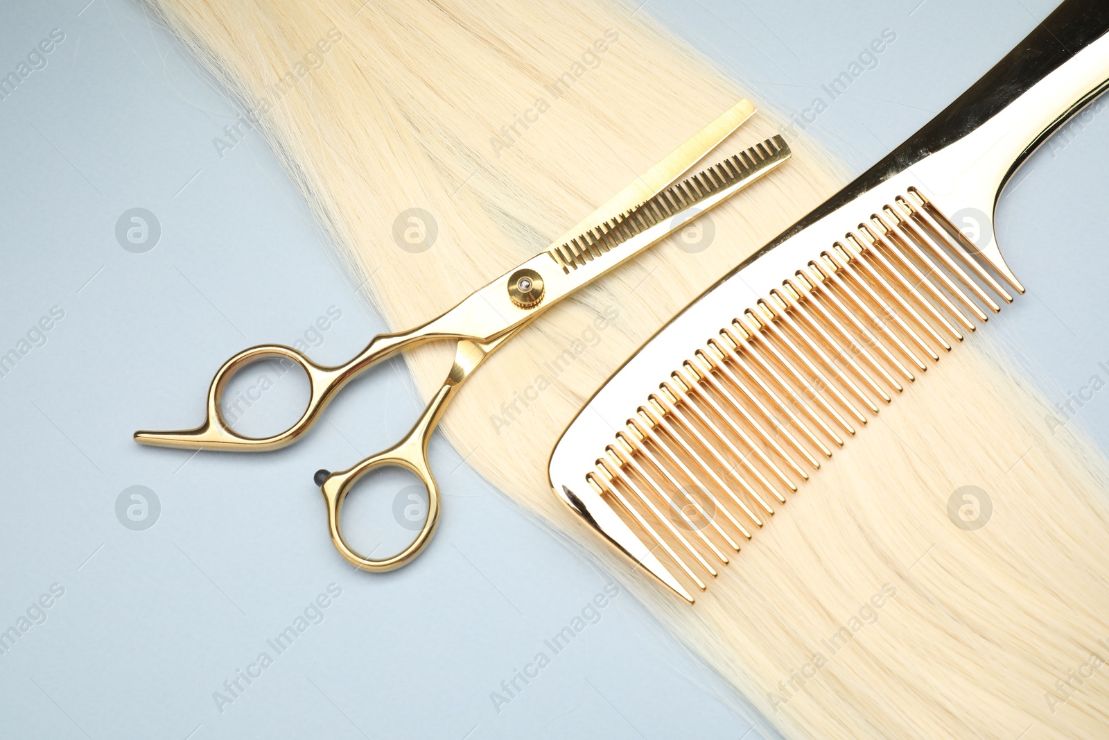 Photo of Blonde hair strand, comb and professional scissors on light grey background, top view