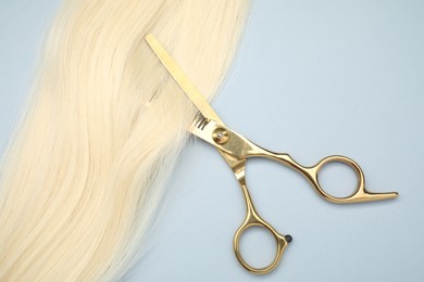 Photo of Blonde hair strand and professional scissors on light grey background, top view