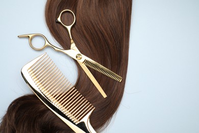 Photo of Brown hair strand, comb and professional scissors on light grey background, top view