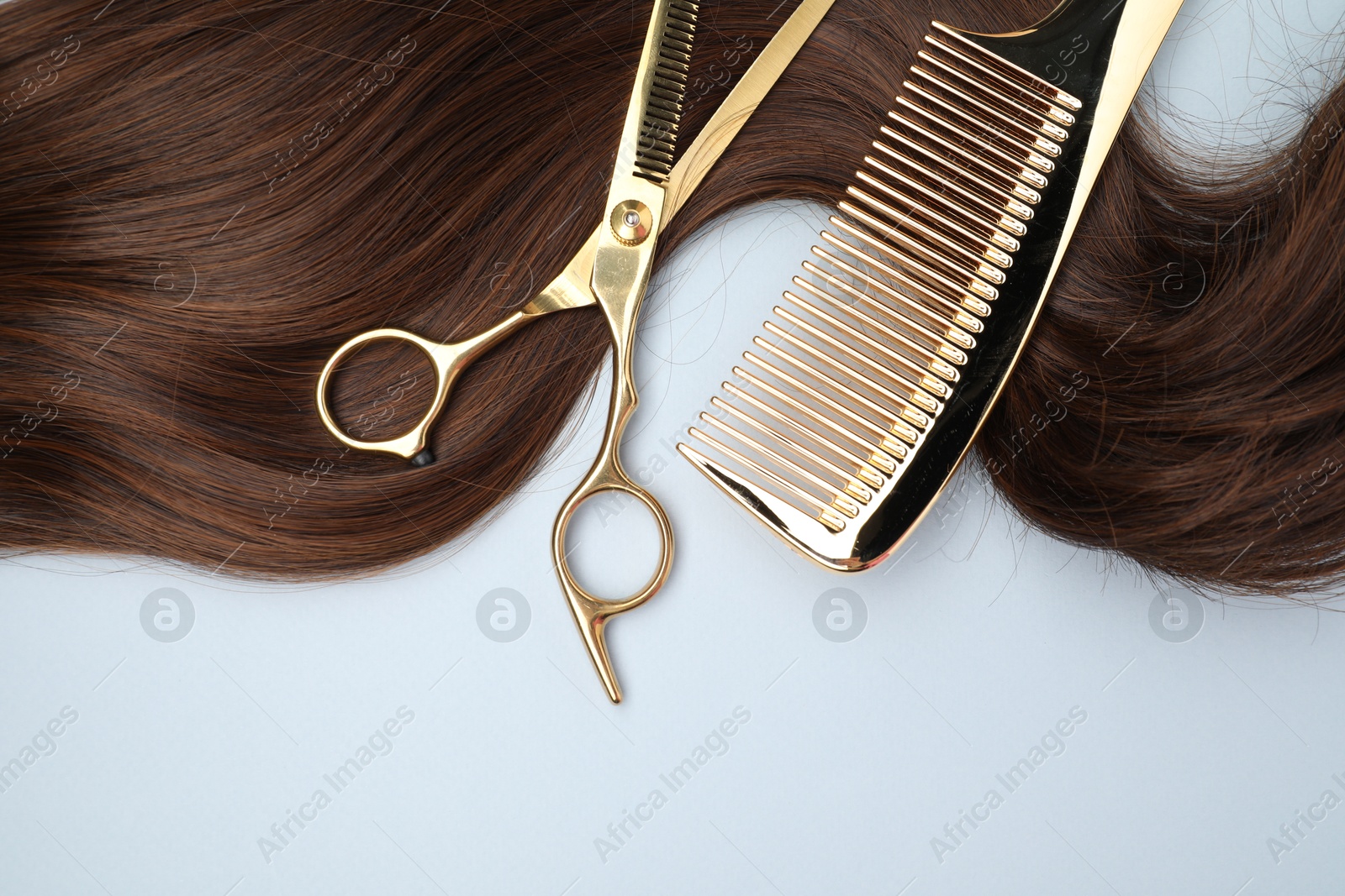 Photo of Brown hair strand, comb and professional scissors on light grey background, top view