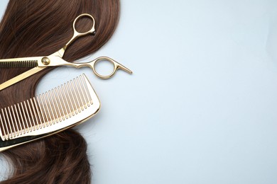 Brown hair strand, comb and professional scissors on light grey background, top view. Space for text