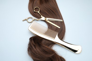 Photo of Brown hair strand, comb and professional scissors on light grey background, top view