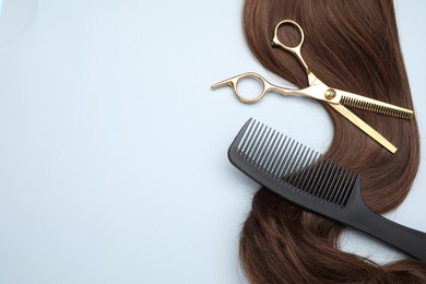 Photo of Brown hair strand, comb and professional scissors on light grey background, top view. Space for text