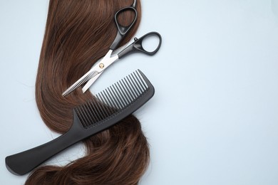 Photo of Brown hair strand, comb and professional scissors on light grey background, top view. Space for text