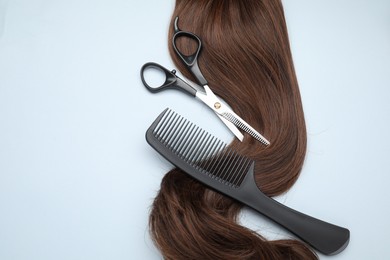 Brown hair strand, comb and professional scissors on light grey background, top view