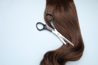 Photo of Brown hair strand and professional scissors on light grey background, top view. Space for text