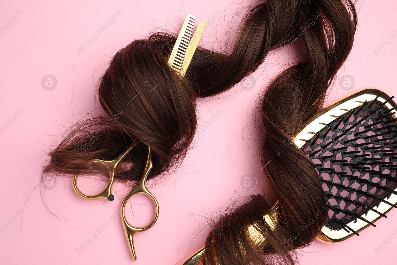 Photo of Brown hair strand, brush and professional scissors on pink background, top view