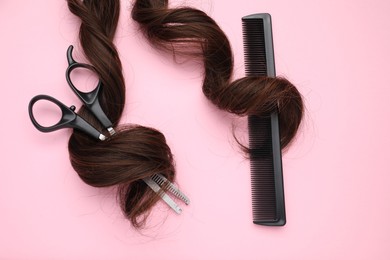 Photo of Brown hair strand, comb and professional scissors on pink background, top view