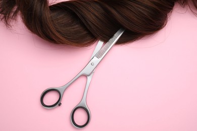 Photo of Brown hair strand and professional scissors on pink background, top view