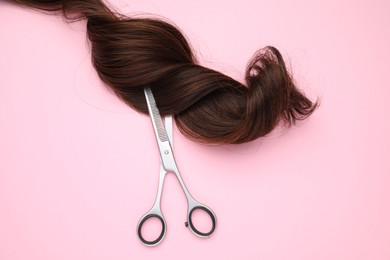 Brown hair strand and professional scissors on pink background, top view