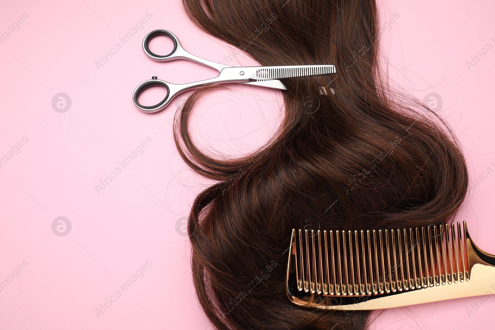 Photo of Brown hair strand, comb and professional scissors on pink background, top view