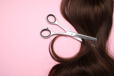 Brown hair strand and professional scissors on pink background, top view