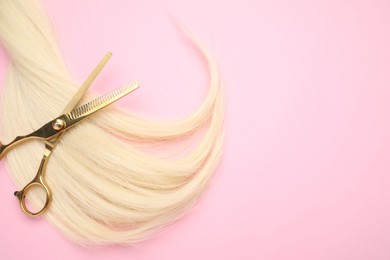 Blonde hair strand and professional scissors on pink background, top view. Space for text