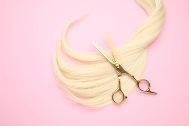 Photo of Blonde hair strand and professional scissors on pink background, top view