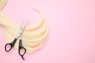 Photo of Blonde hair strand and professional scissors on pink background, top view. Space for text