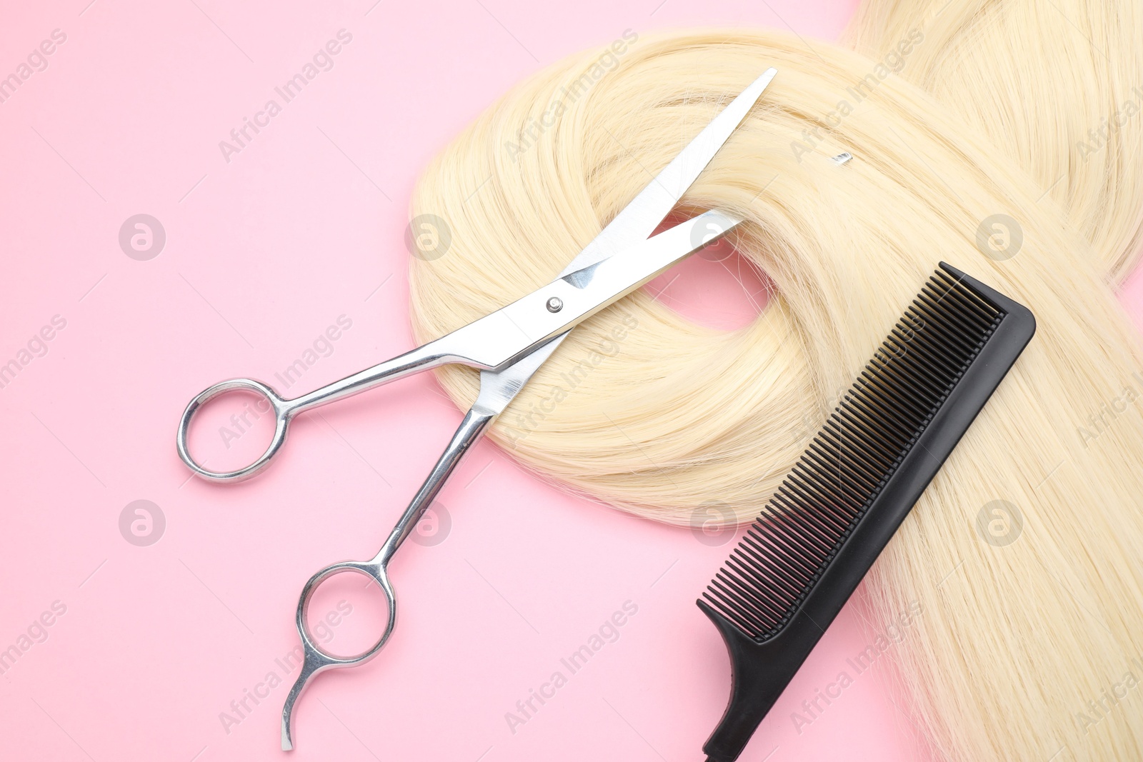 Photo of Blonde hair strand, comb and professional scissors on pink background, top view