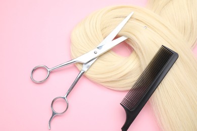 Blonde hair strand, comb and professional scissors on pink background, top view