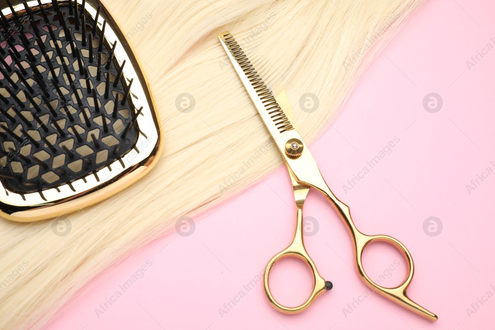 Photo of Blonde hair strand, brush and professional scissors on pink background, top view