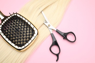 Blonde hair strand, brush and professional scissors on pink background, top view