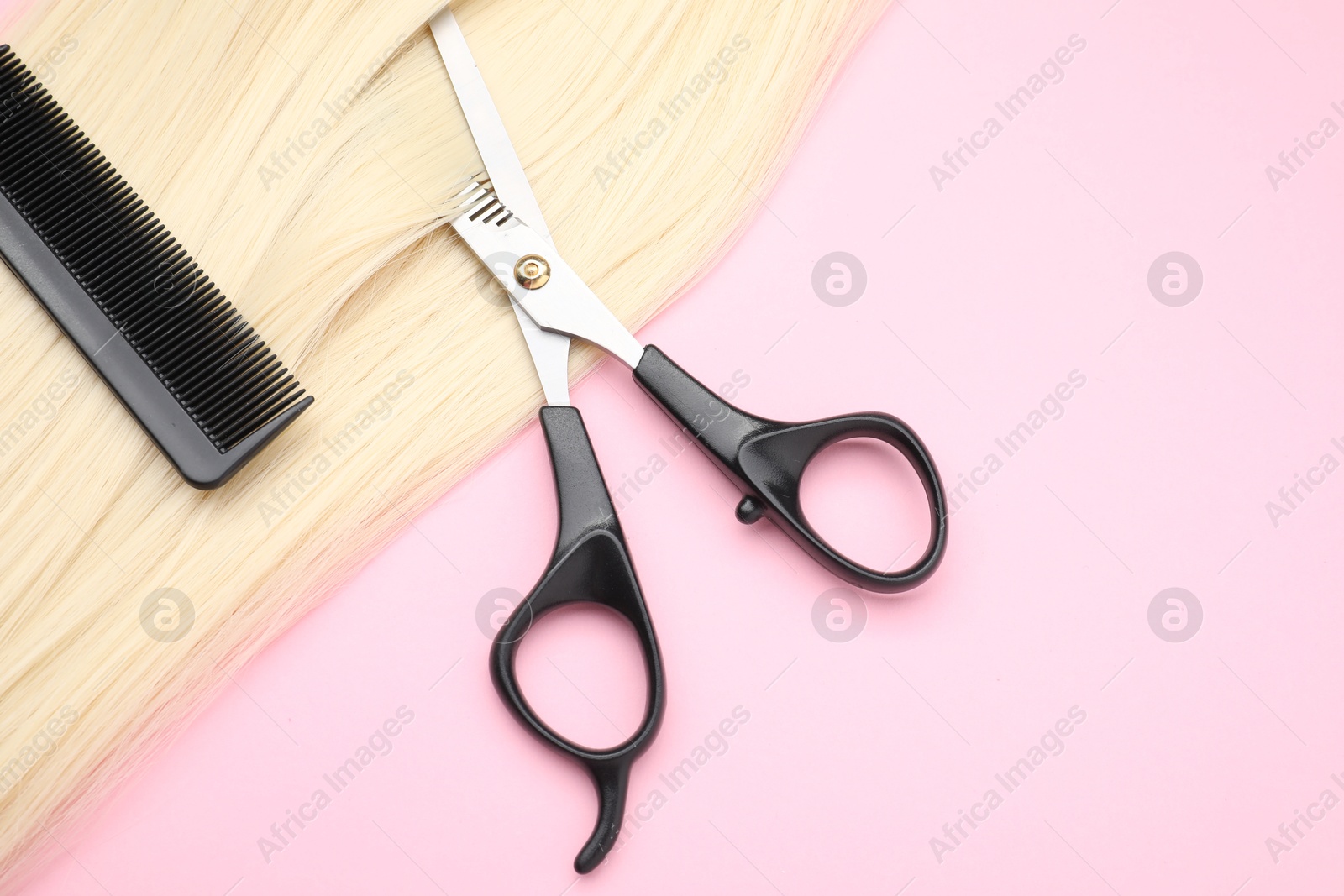 Photo of Blonde hair strand, comb and professional scissors on pink background, top view