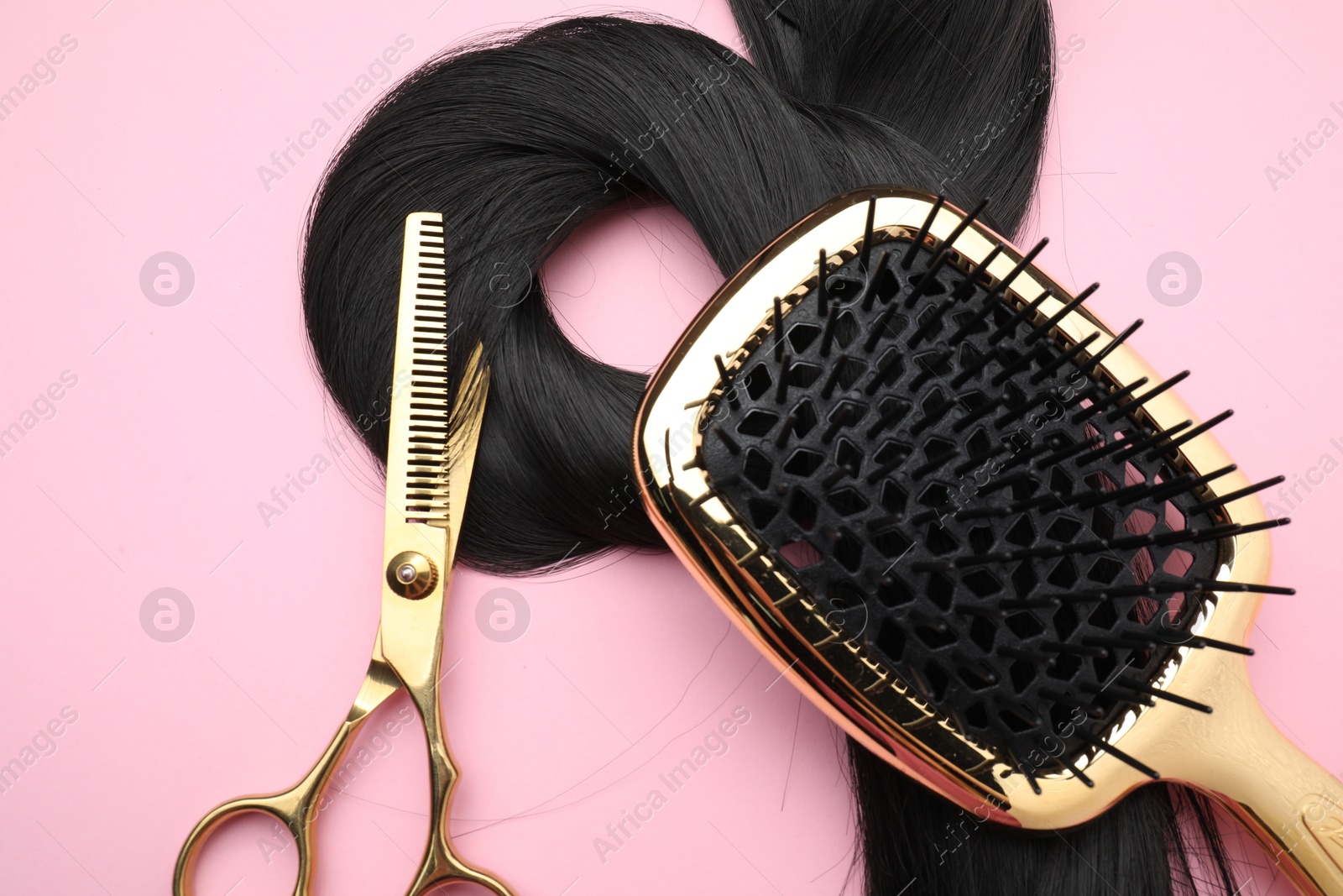 Photo of Black hair strand, brush and professional scissors on pink background, top view