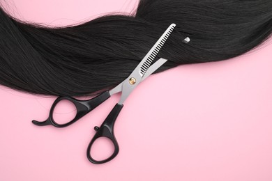 Photo of Black hair strand and professional scissors on pink background, top view