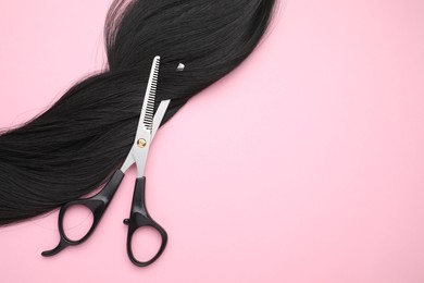 Photo of Black hair strand and professional scissors on pink background, top view. Space for text