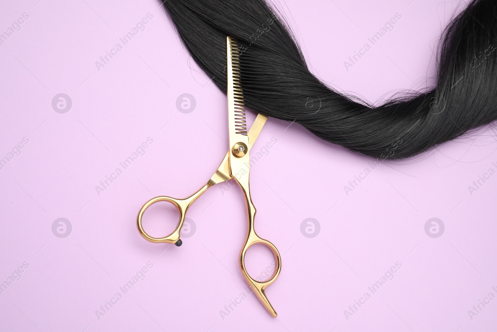 Photo of Black hair strand and professional scissors on pink background, top view