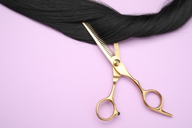 Photo of Black hair strand and professional scissors on pink background, top view