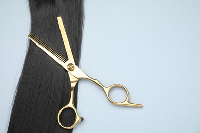 Black hair strand, comb and professional scissors on light grey background, top view