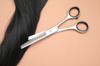 Black hair strand and professional scissors on pale coral background, top view