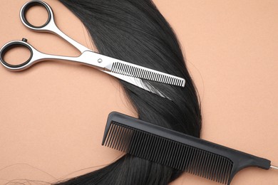 Black hair strand, comb and professional scissors on pale coral background, above view