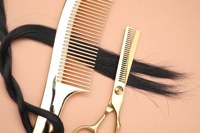 Photo of Black hair strand , comb and professional scissors on pale coral background, top view