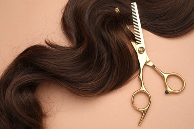 Brown hair strand and professional scissors on pale coral background, top view