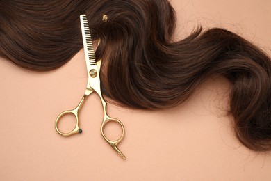 Brown hair strand and professional scissors on pale coral background, top view