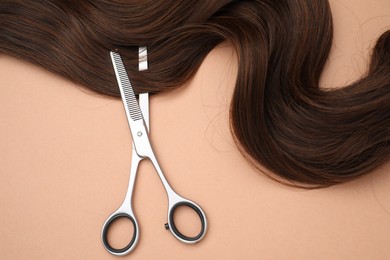 Brown hair strand and professional scissors on pale coral background, top view