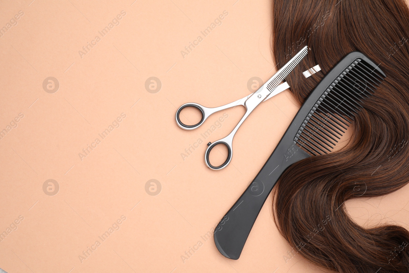 Photo of Brown hair strand, comb and professional scissors on pale coral background, top view. Space for text