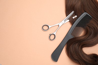 Photo of Brown hair strand, comb and professional scissors on pale coral background, top view. Space for text