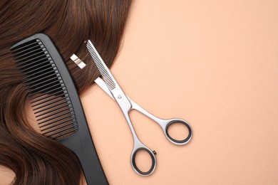 Brown hair strand, comb and professional scissors on pale coral background, top view