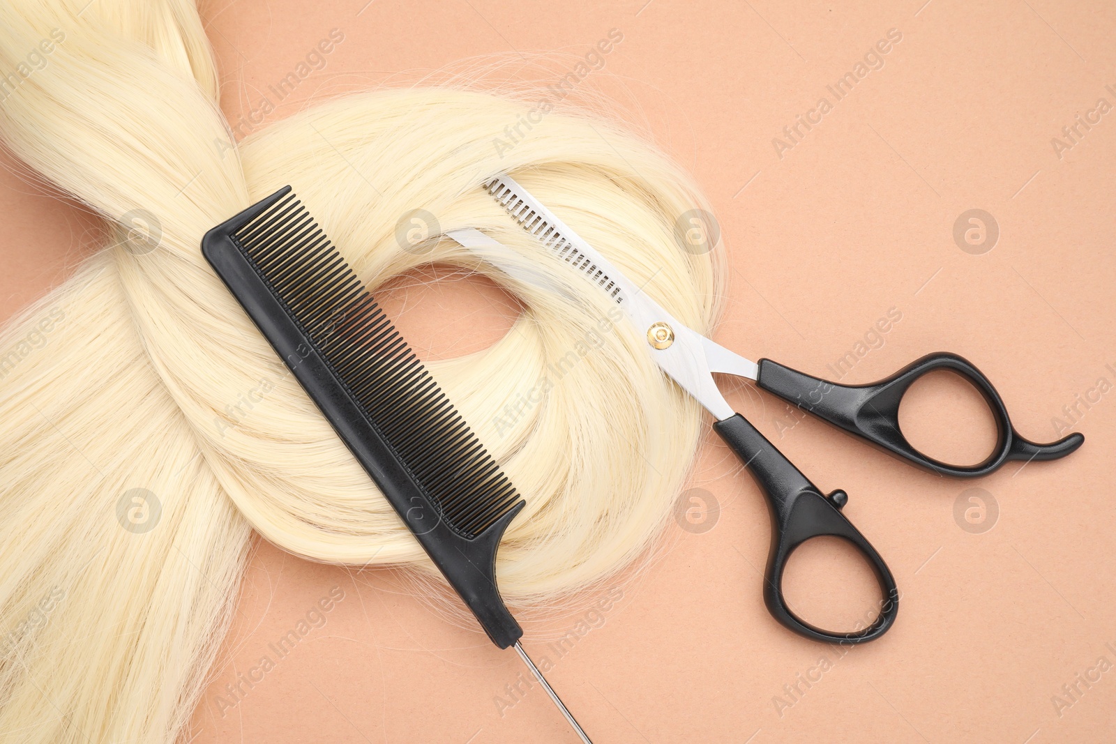 Photo of Blonde hair strand, comb and professional scissors on pale coral background, top view