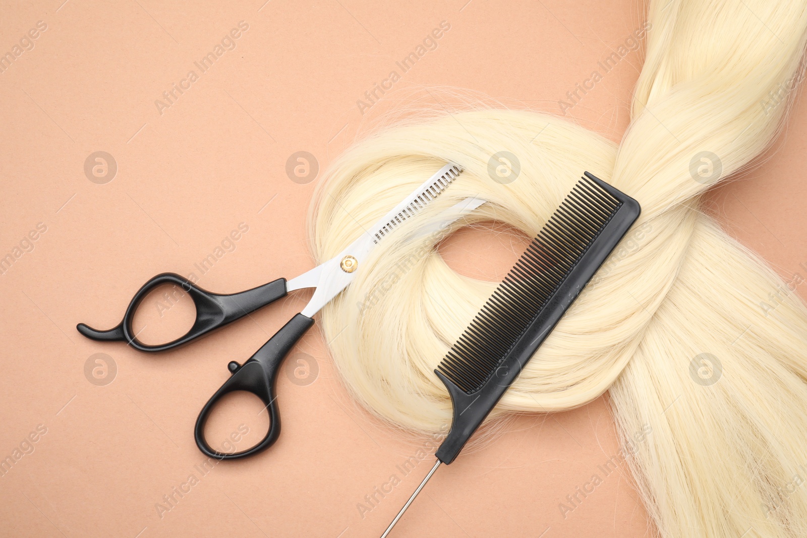 Photo of Blonde hair strand, comb and professional scissors on pale coral background, top view