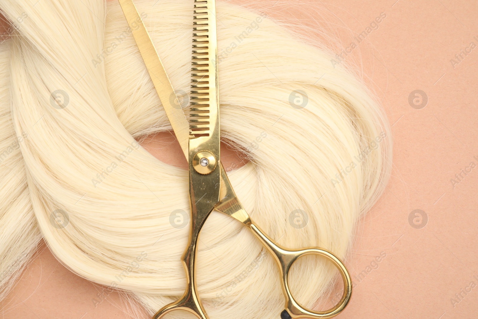 Photo of Blonde hair strand and professional scissors on pale coral background, top view