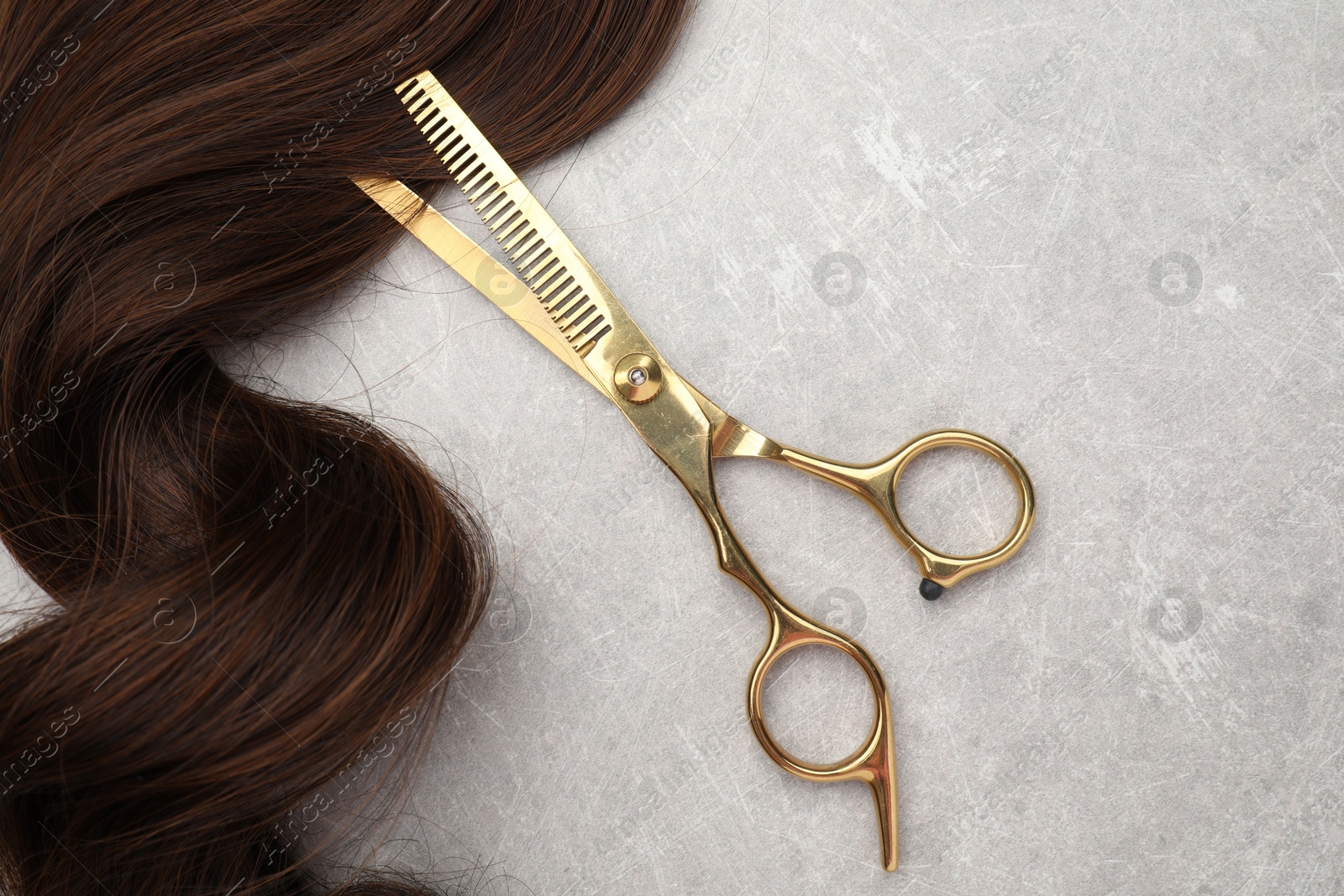 Photo of Brown hair strand and professional scissors on grey table, top view