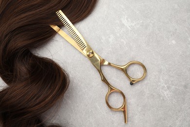 Photo of Brown hair strand and professional scissors on grey table, top view