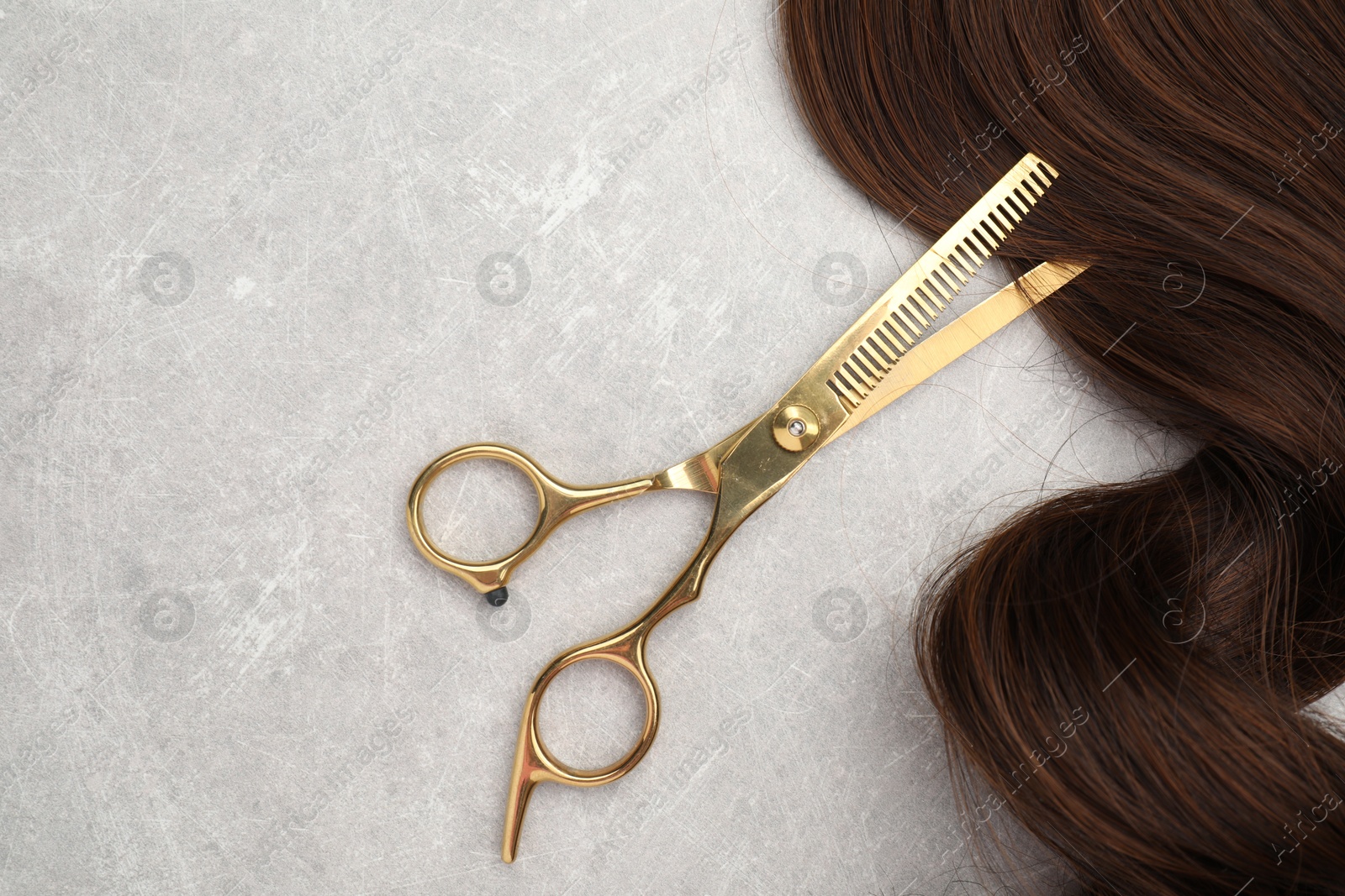 Photo of Brown hair strand and professional scissors on grey table, top view