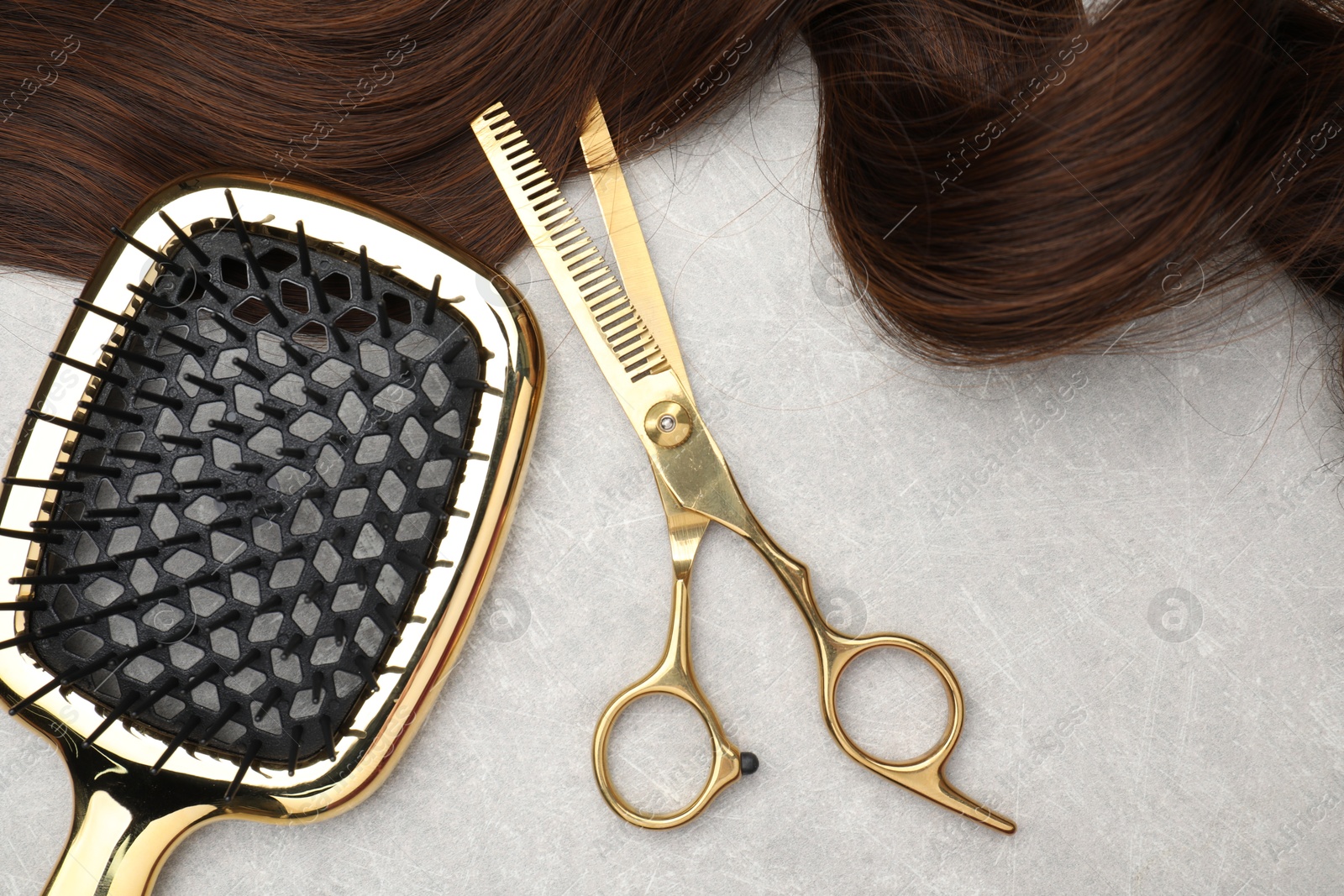 Photo of Brown hair strand, brush and professional scissors on grey table, top view