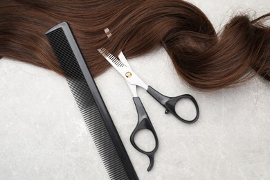 Photo of Brown hair strand, comb and professional scissors on grey table, top view