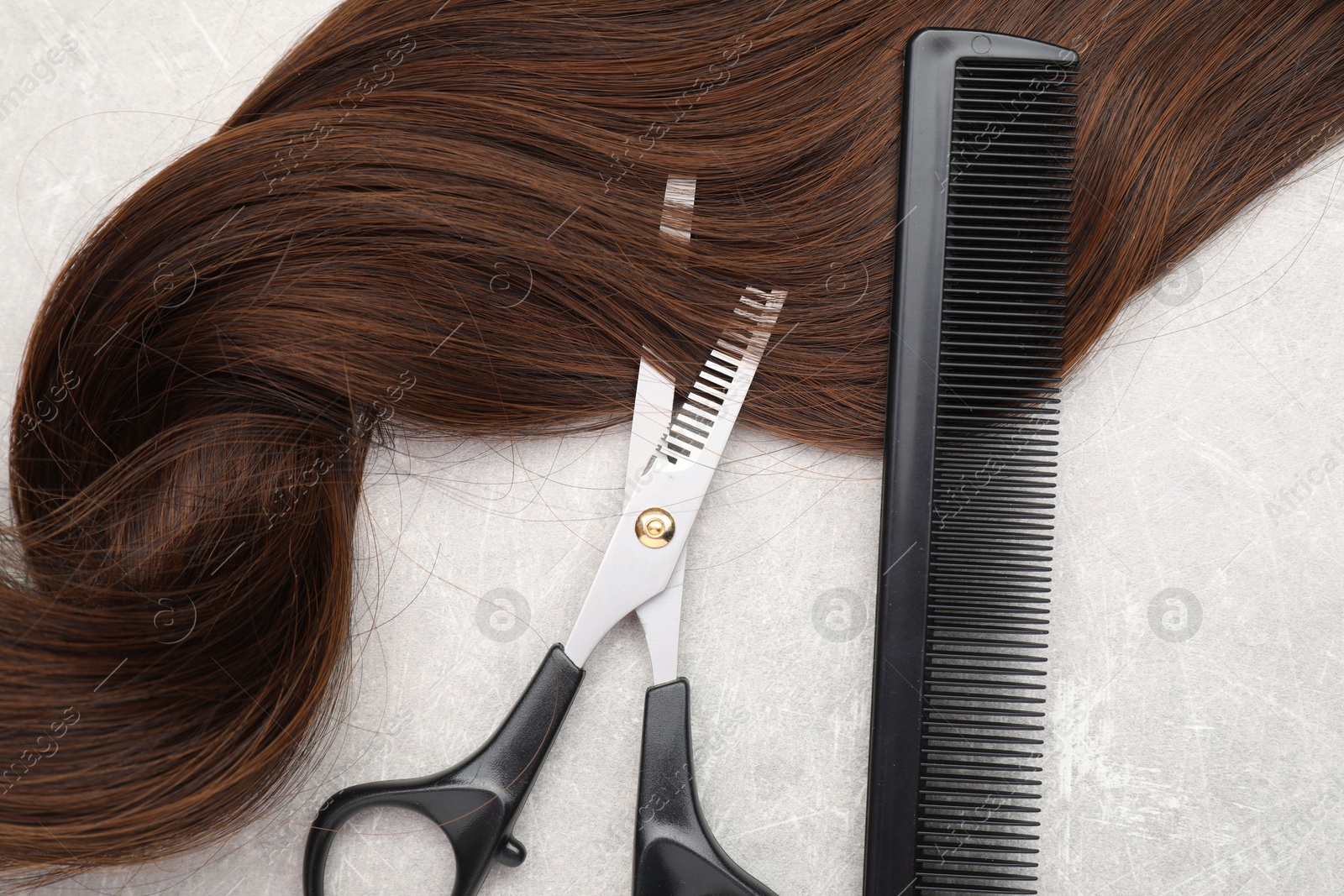 Photo of Brown hair strand, comb and professional scissors on grey table, top view